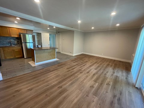 A spacious room with wooden flooring and a kitchen area with a refrigerator and cabinets.
