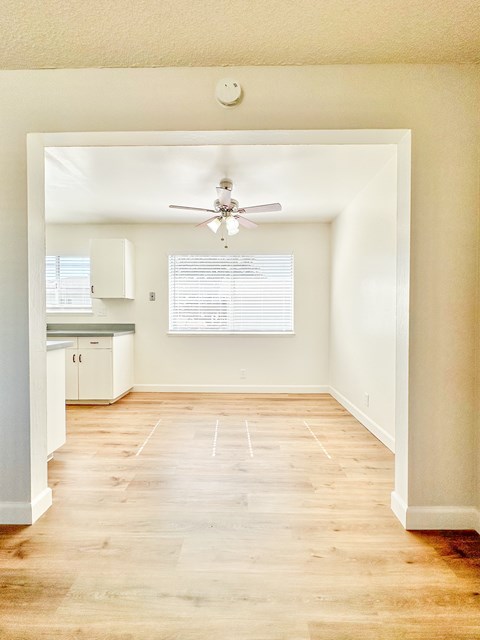 an empty living room with a ceiling fan and a kitchen