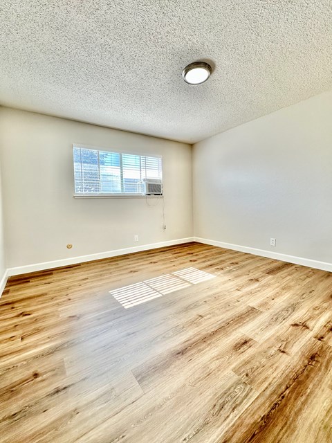 an empty living room with wood flooring and a window