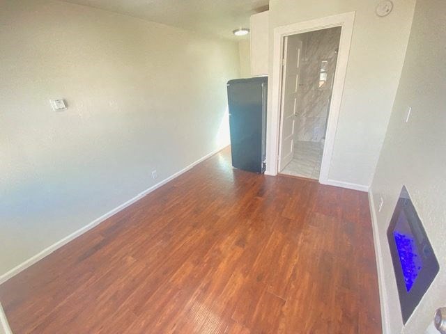 A black refrigerator sits in a room with wooden floors.