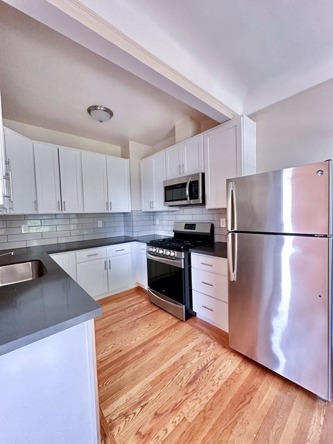 A kitchen with a stainless steel refrigerator and wooden floors.