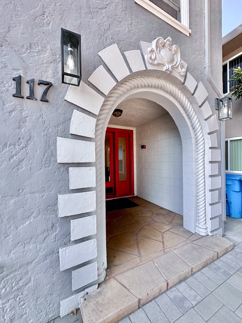 A white building with a red door and a number 117 on the wall.