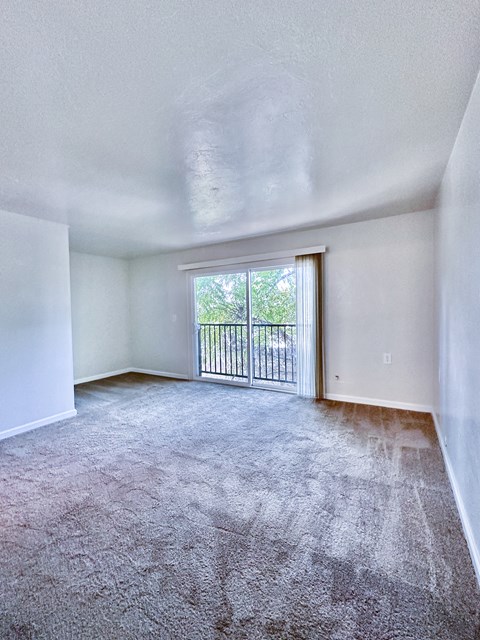 an empty living room with a sliding glass door to a balcony
