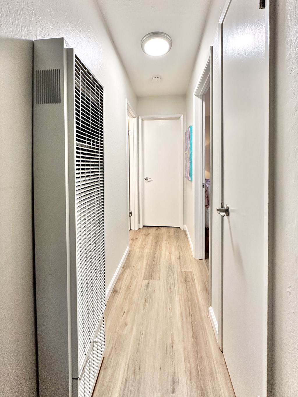 a long hallway with white walls and wood flooring and a closet