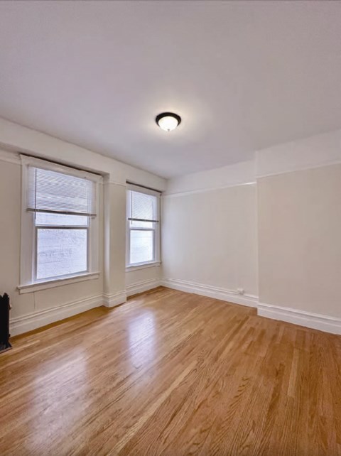an empty living room with a wooden floor and two windows