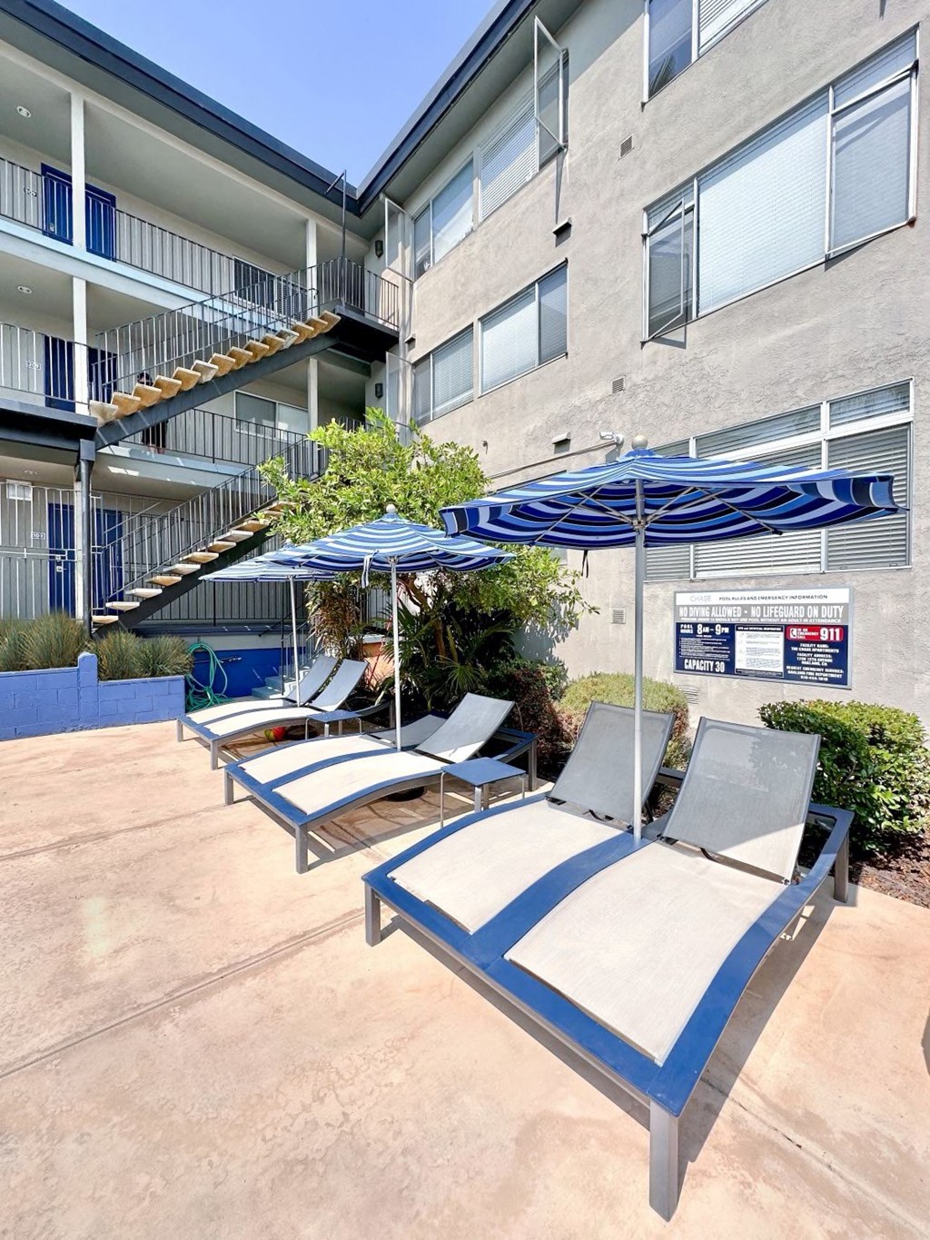 a patio with lounge chairs and umbrellas in front of an apartment building