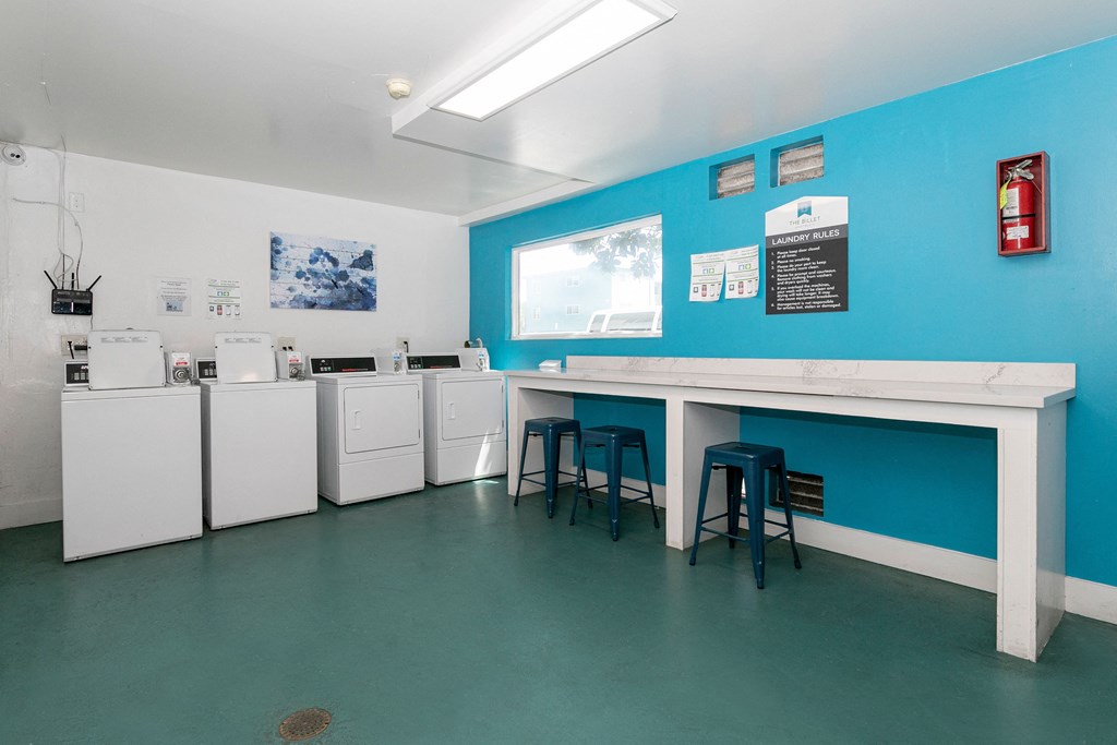 a break room with a counter and stools and a blue wall and white appliances