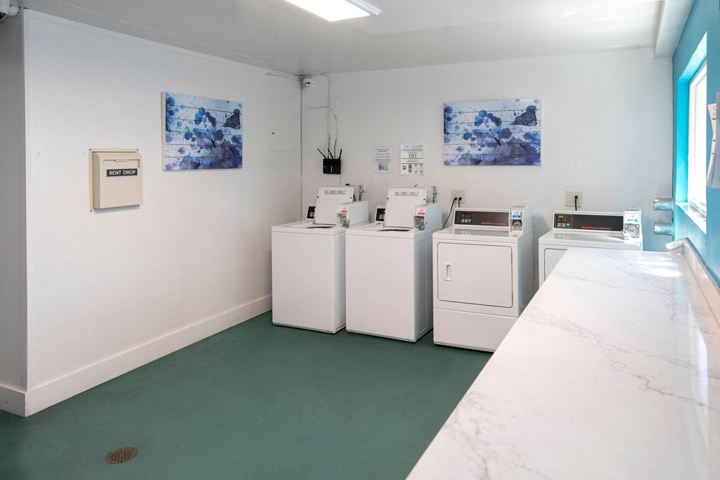 a laundry room with four washes and a counter with a sink and a window