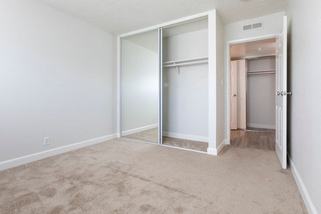 an empty bedroom with a closet with mirrored doors