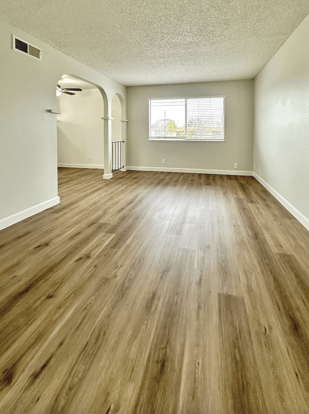 A room with wooden flooring and a window showing a view of a fence and trees.