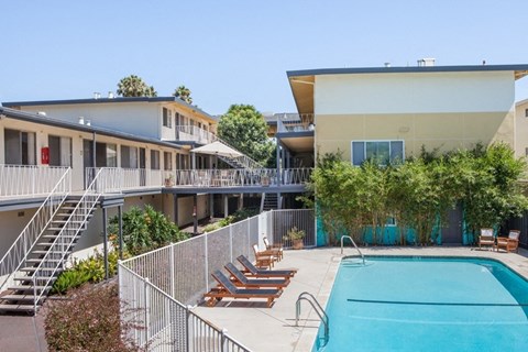 A pool area with sun loungers and a building in the background.