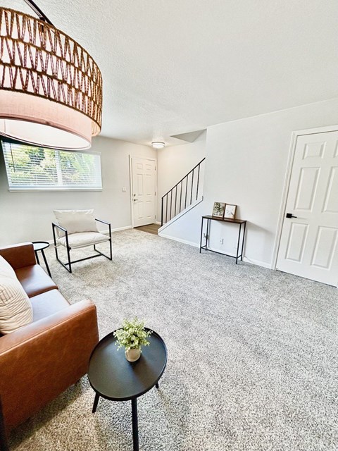 A living room with a brown couch, a small table with a plant on it, and a staircase in the background.