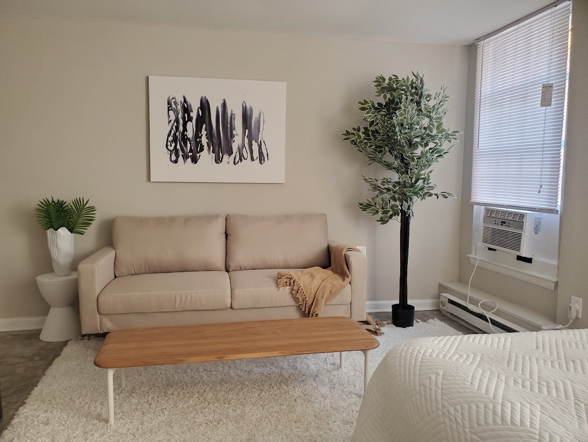 A living room with a beige couch, a white rug, and a painting on the wall.