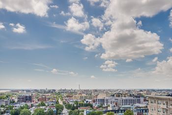 A cityscape with buildings and trees under a blue sky with clouds.
