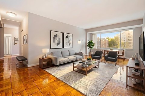A living room with a grey sofa, a grey couch, a grey chair, a grey rug, a grey coffee table, a grey floor lamp, a grey wall, a grey door, a grey wall, a grey wall, a grey