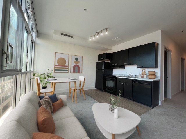 A modern living room with a grey sofa, a white coffee table, and a kitchen area in the background.