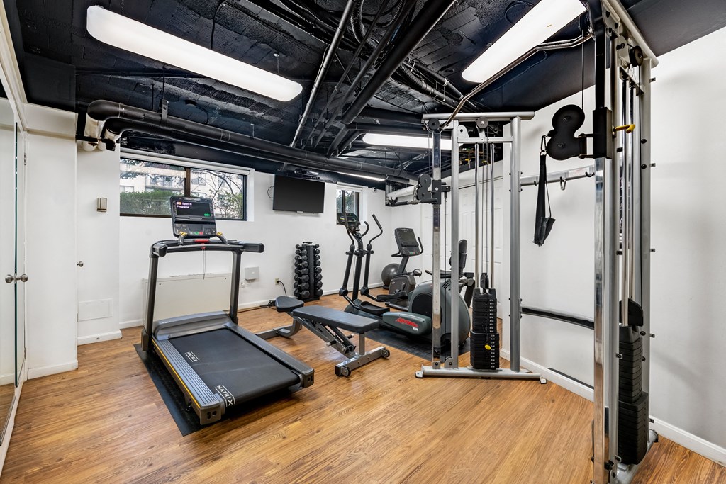 a gym with exercise equipment and weights in a room with white walls and wood floors