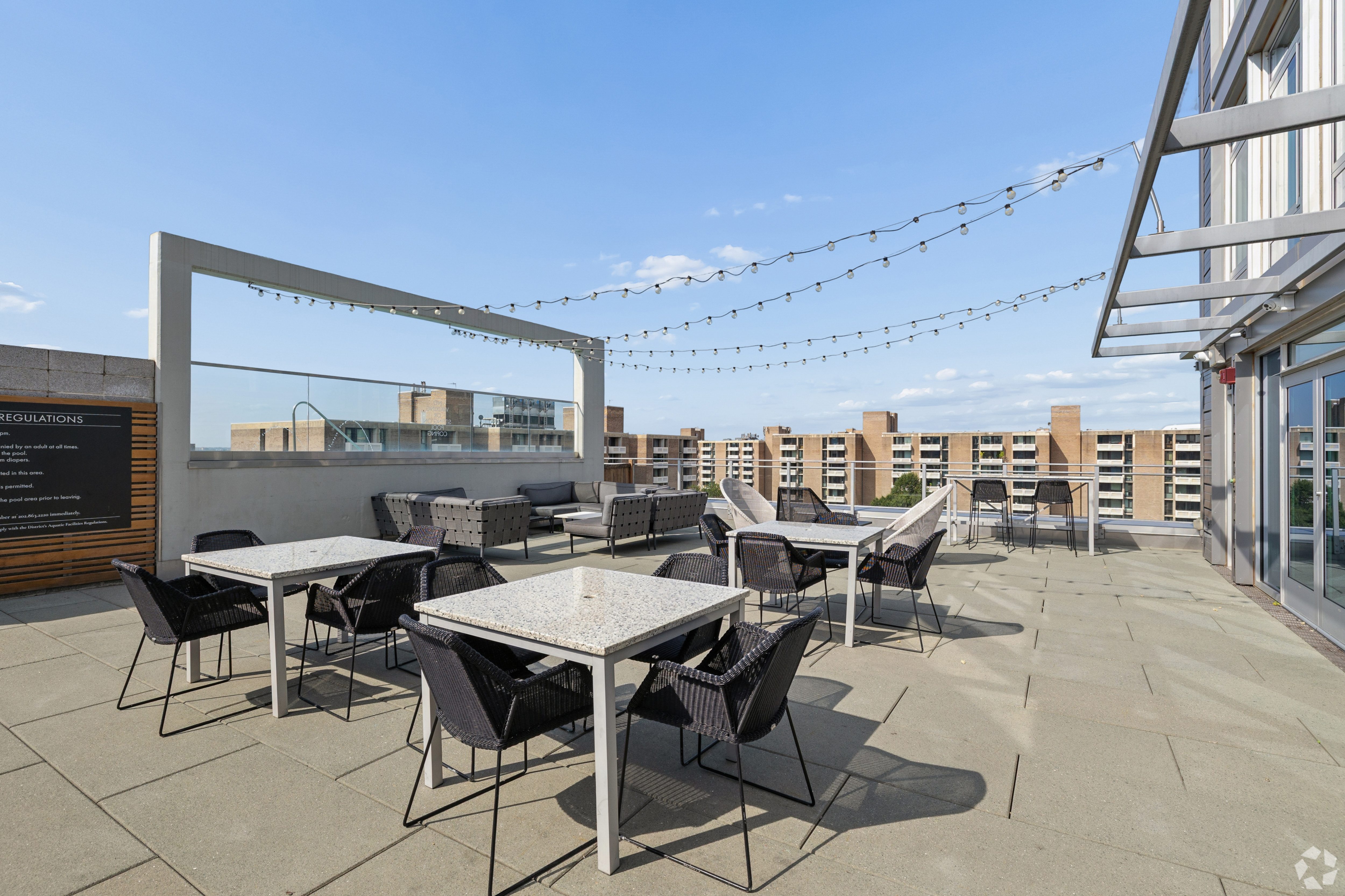 A rooftop patio with tables and chairs and string lights.