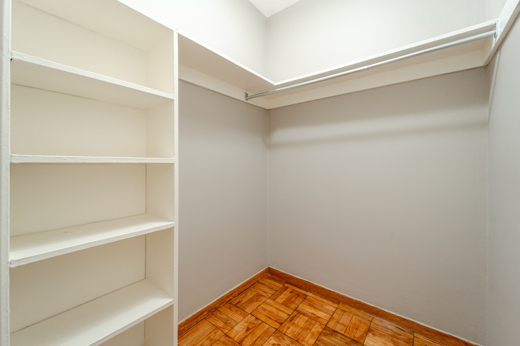 a walk in closet in a home with gray walls and a wooden floor