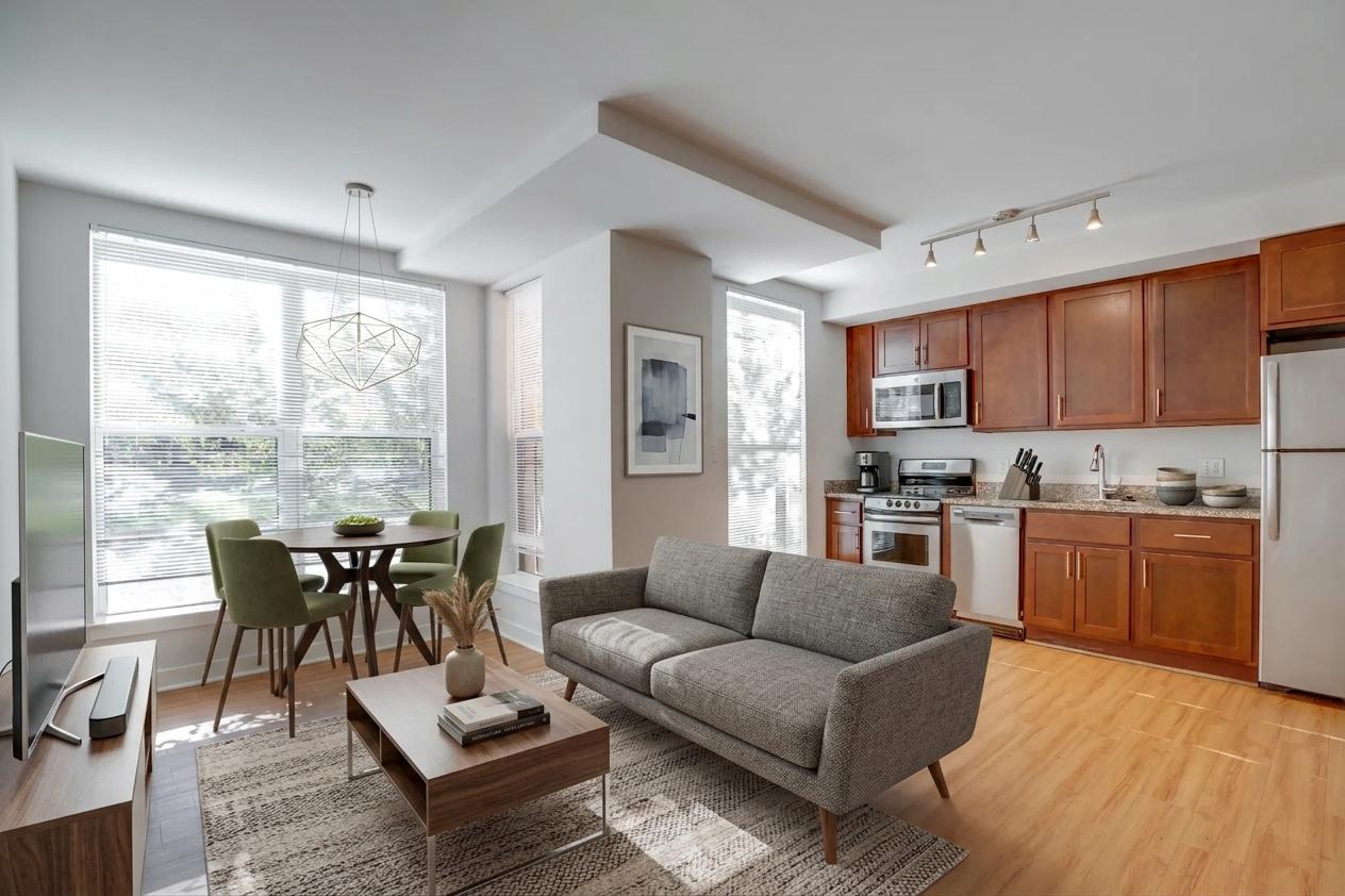 A modern living room with a grey sofa, a wooden coffee table, and a dining table with chairs.