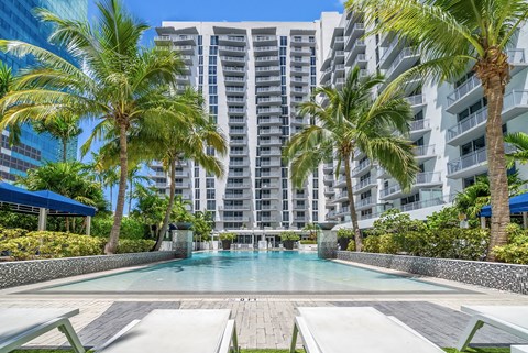 A pool surrounded by palm trees and a building in the background.