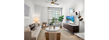 A living room with a couch, a chair, a table, a television, and a ceiling fan.