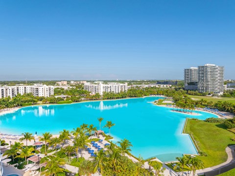 A large swimming pool surrounded by palm trees and a resort.