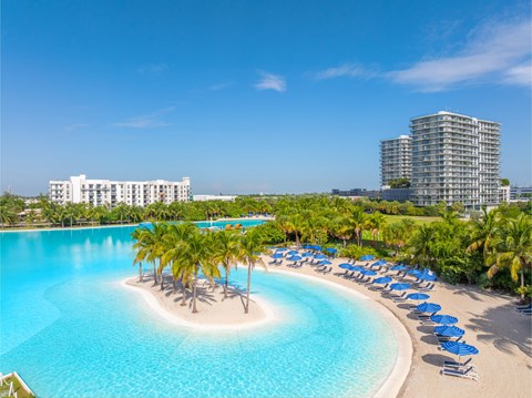 A large swimming pool with a small island in the middle and palm trees around it.
