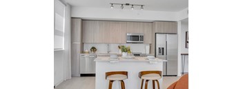 A modern kitchen with a white countertop and wooden chairs.