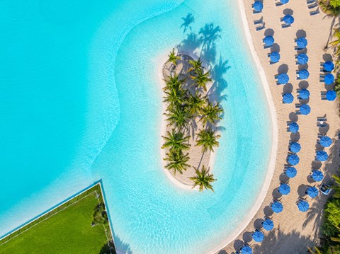 A beautiful beach with a small island surrounded by blue umbrellas.