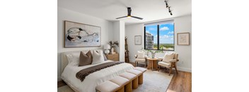 A bedroom with a large bed and a view of a building outside the window.