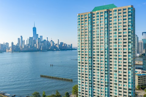 A tall building with a green roof is in the foreground with a city skyline in the background.