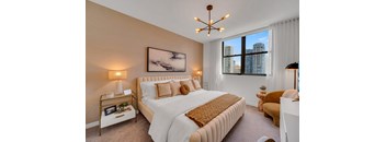 A bedroom with a large bed, a painting on the wall, and a window with a view of the city.