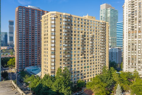 A tall building with many windows is in the foreground of a cityscape.