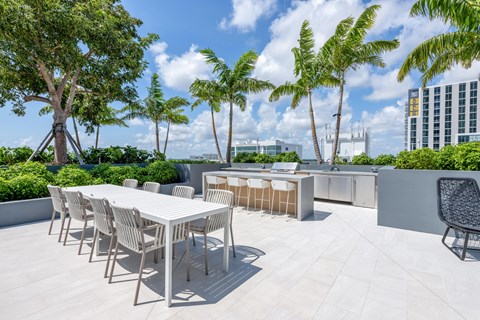 A white table and chairs are set up on a rooftop patio with trees in the background.