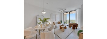 A modern living room with a dining table set for two and a view of the balcony.