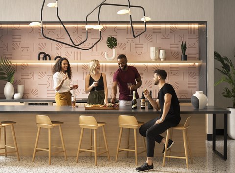 Four people are standing in a kitchen with a pink wallpaper.