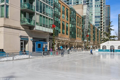 People skate on an outdoor ice rink in front of a building.