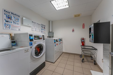 A laundry room with a washing machine, dryer, and a shopping cart.
