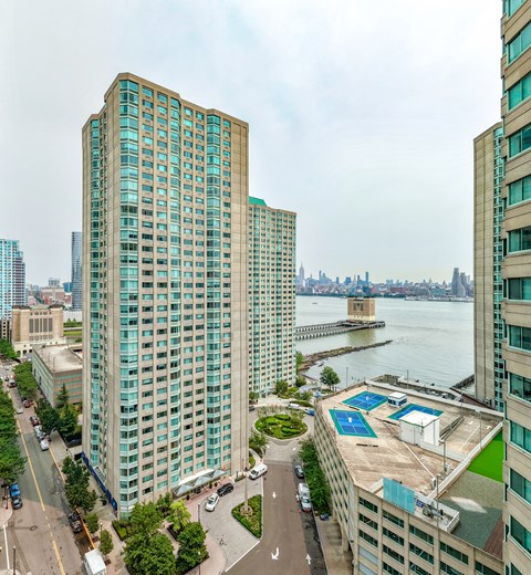 A view of a cityscape with a large body of water in the background and a green space with a tennis court in the foreground.