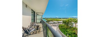A balcony with chairs and a table overlooks a pool and greenery.