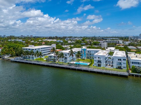 A large white building with a pool is situated on the edge of a body of water.