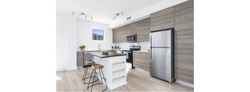 A modern kitchen with a refrigerator, microwave, and bar stools.