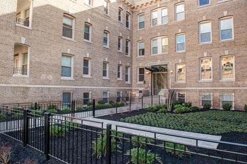 A large brick building with a black fence and a garden in front.