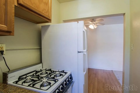A white refrigerator with a black handle is in a kitchen with a stove and wooden cabinets.