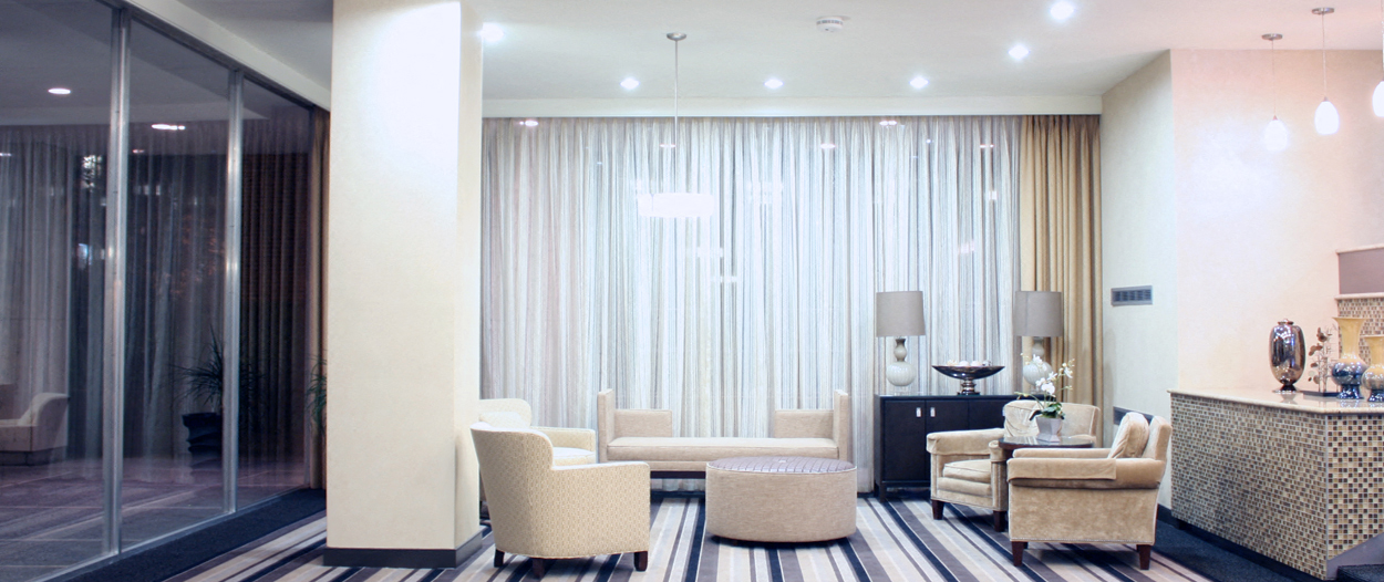 the living room of a hotel suite with white curtains and chairs