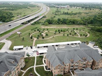 A highway curves through a green landscape with a parking lot and apartment buildings.