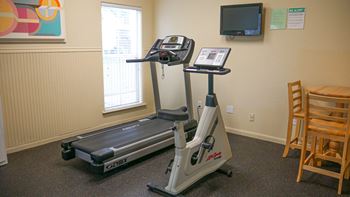 A treadmill and a stationary bike are in a room with a TV and a chair.