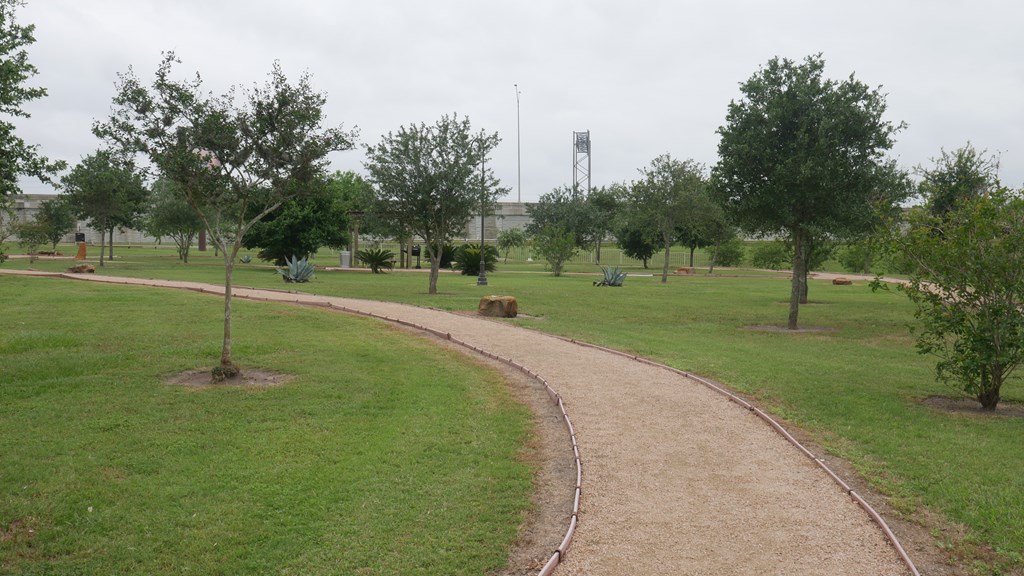 A park with a dirt path and green grass.