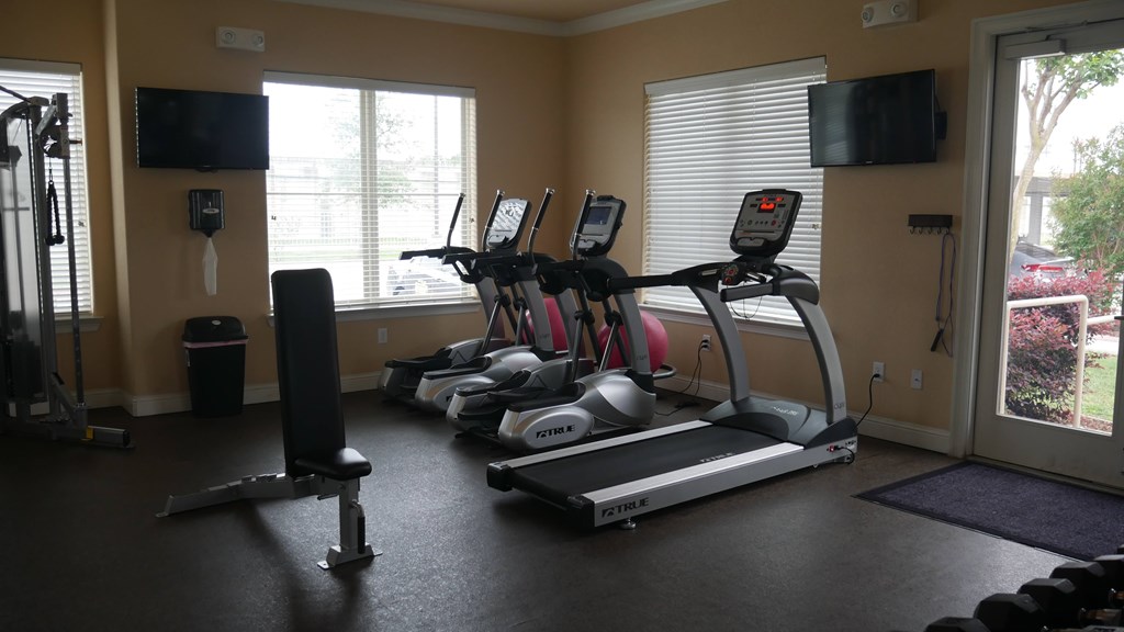 A gym with treadmills, a weight bench, and a television.